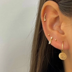 Detail of multiple S925 silver ear piercings with crystal studs and gold coin hoop earring