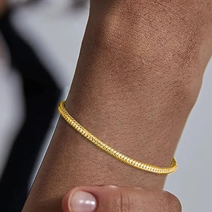 Close-up of a gold snake bone chain bracelet worn on a wrist with metallic luster