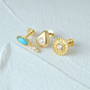 Detailweergave van drie gouden S925 zilveren piercings met turkoois en zirkoon steentjes