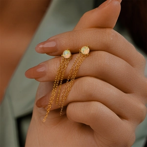 Macro detail of S925 silver gold-plated opal tassel earrings held in hand