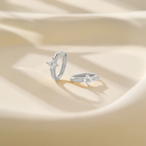 Detailed view of silver flower huggie earrings with cubic zirconia on satin background