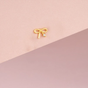 Détail de la boucle d'oreille nœud en or mat avec petit zircon sur fond rose pastel