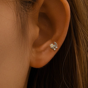 Vue macro d'un piercing lune et étoile en argent avec opale colorée sur le cartilage
