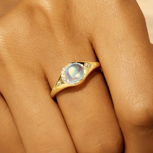 Nahaufnahme eines eleganten Goldrings mit Mondstein und Diamanten am Finger