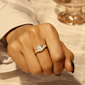 Detail eines eleganten Goldrings mit Mondstein und kleinen Diamanten an der Hand getragen