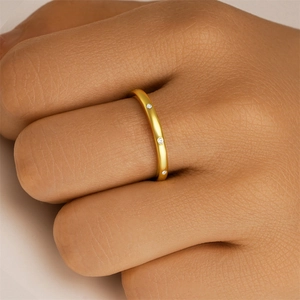 Detailansicht eines goldmattierten Rings mit drei kleinen eingelassenen Diamanten am Finger