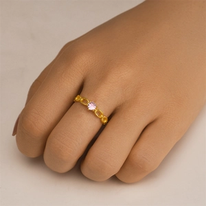 Detail of a golden chain-style ring with a six-prong set pink gemstone on a finger