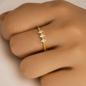 Detail of a golden beaded floral ring with sparkling zircon inlays on a model's finger