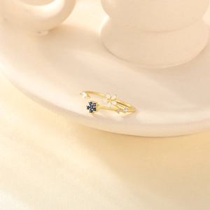 Detail of adjustable gold floral ring featuring white enamel and blue crystal flowers