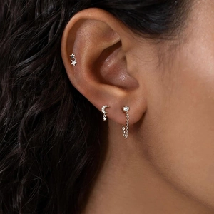 Macro shot of S925 silver four-petal flower and star stud earrings on a model's ear