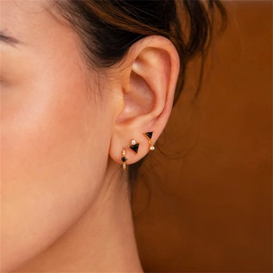 Detailed view of three gold flower earrings with black stones and crystals on a model