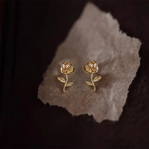 Makroaufnahme goldener Rosen-Ohrstecker mit detaillierten Blütenblättern auf Vintage-Papier