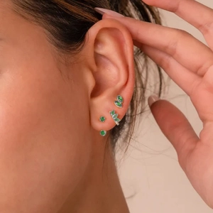 Close-up of emerald green four-petal flower earrings set in gold on female ear