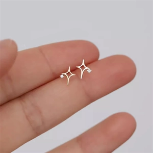 Nahaufnahme kleiner goldener Stern-Ohrstecker mit funkelndem Zirkon zwischen den Fingern