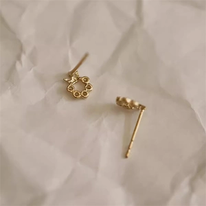 Nahaufnahme von goldenen Kronen-Kranz-Ohrsteckern auf minimalistischem Papierhintergrund
