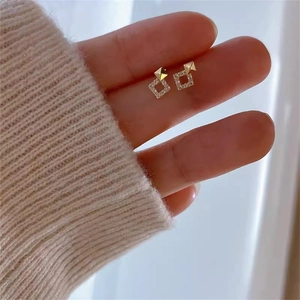 Detail von goldenen geometrischen Ohrringen mit Zirkonia vor weichem Strickhintergrund