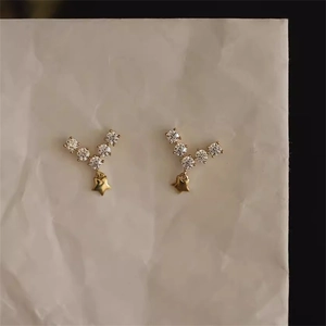 Detailansicht der goldenen Ohrringe mit V-förmigen Kristallen und kleinen Sternanhängern
