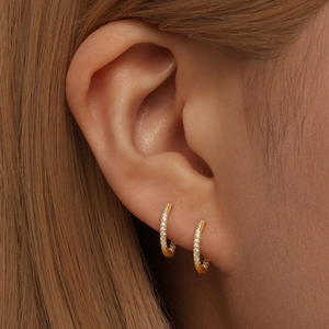 Macro shot of gold hoop earrings with white crystals on a woman's earlobe