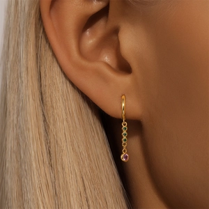 Detail of gold huggie hoop earring with bezel-set green and pink gems on model