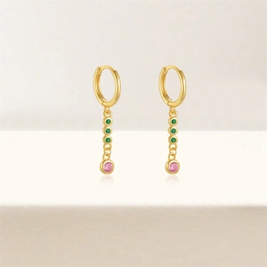 Detail of gold hoop earrings featuring green and pink bezel-set gemstones on white base