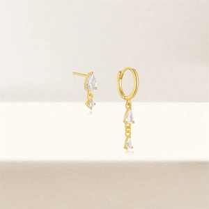 Detailed view of asymmetric gold-plated earrings with clear pear-cut crystals