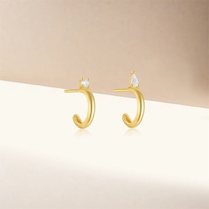 Detail of gold-plated asymmetric C-shaped hoop earrings featuring round and pear-cut zircons