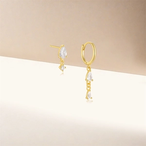 Detailed shot of asymmetrical gold earrings featuring pear-shaped zircon stones