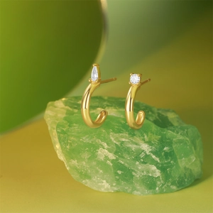 Detail of C-shape gold earrings with pear and round cut crystals on green stones