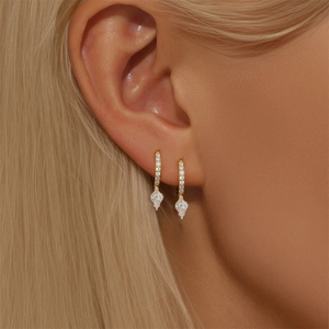 Close-up of golden diamond-encrusted earrings with cat eye stones on a model ear