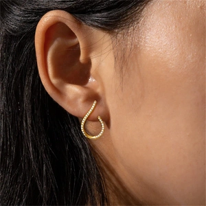 Close-up of gold curved earrings with pavé diamonds worn on a model's earlobe