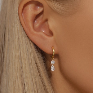 Macro shot of gold hoop earrings with round and teardrop zircons worn by model
