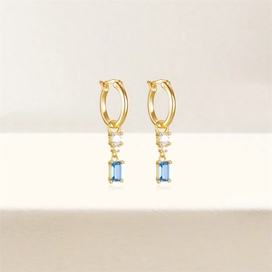 Detail of gold hoop earrings with sparkling round diamonds and light blue rectangular stones