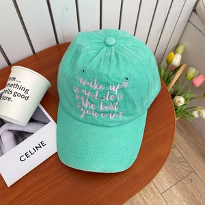 Close-up of mint green washed cotton cap with pink embroidered slogan and floral details