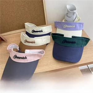 Multiple color variations of Greenich embroidered open top sun visors on a wooden surface