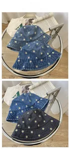 Detailed embroidery of white daisies on denim and twill cotton bucket hats on a glass table