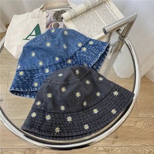 Blue and black denim bucket hats with small daisy embroidery on a minimal glass table
