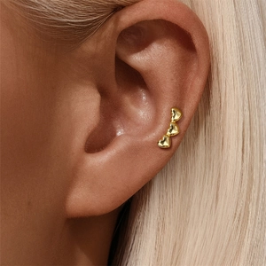 Close-up of three gold-plated hearts stud earrings worn on the ear cartilage