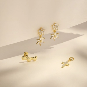 Detail of gold heart studs and floral zircon earrings on a minimalist beige background