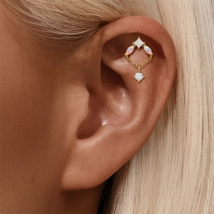 Detailed view of a gold helix cartilage piercing with opal marquise and a dangling zircon