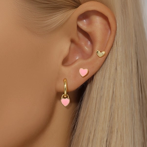Gros plan de boucles d'oreilles cœur rose émaillé et créoles dorées sur l'oreille