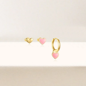 Détail d'un ensemble de trois pièces avec boucles d'oreilles cœur rose et créole dorée sur beige