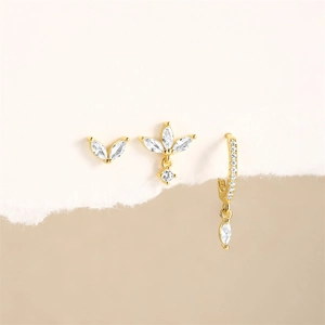 Détail de trois boucles d'oreilles dorées avec motifs de feuilles en zircon marquise