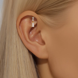 Detail of a gold S925 silver stud earring with three sparkling zircons on a model's ear