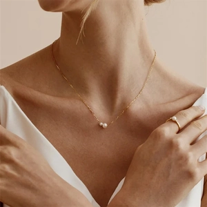 Detalle de un collar minimalista de plata S925 dorada con dos perlas en una modelo