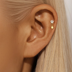 Close-up of a gold star-shaped cartilage stud with pavé zircon and a dangling star charm