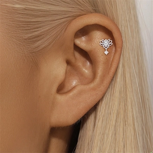 Macro shot of silver lotus piercing earring with sparkling zircons worn on ear lobe