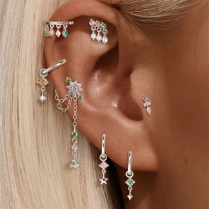 Detail of silver cartilage earrings with colorful zircon stars and long flower chains
