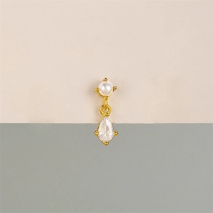 Detail of a gold stud earring with a round white pearl and a pear-cut clear zircon stone