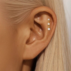 Detail of three graduating white zircon stones in gold stud earring on an ear