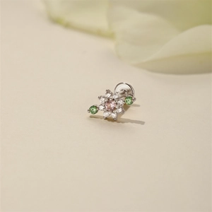 Macro shot of silver flower piercing with pink center gem and green accents